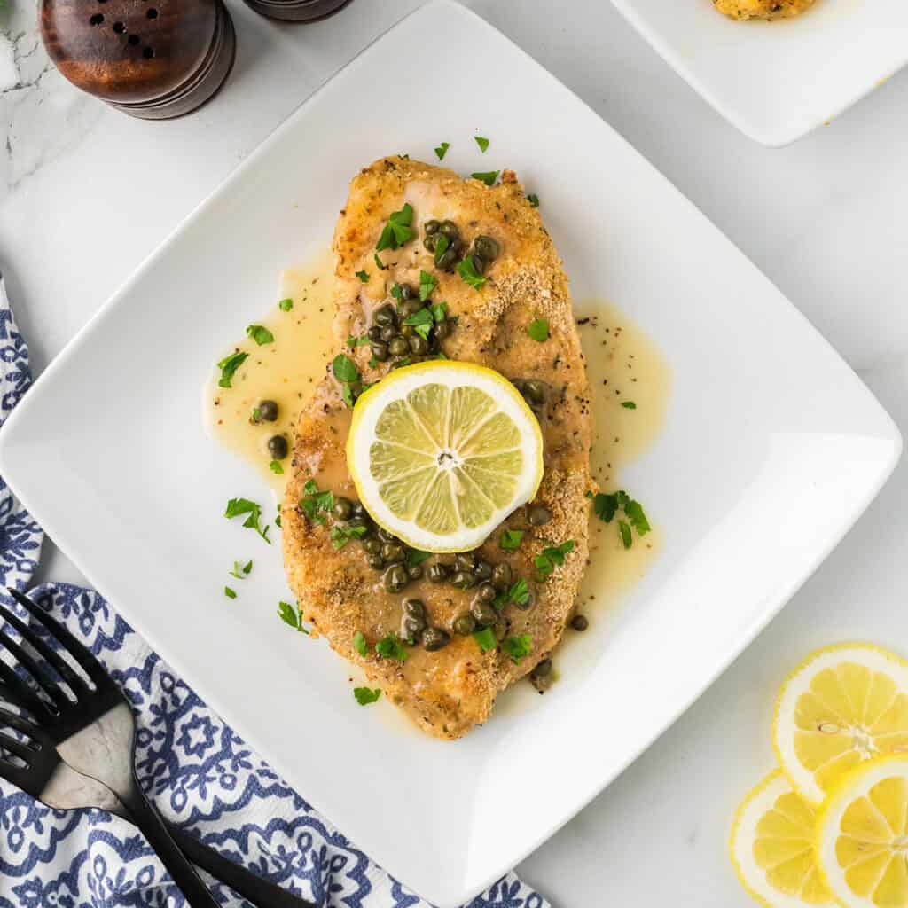 A serving of chicken piccata on a white plate.