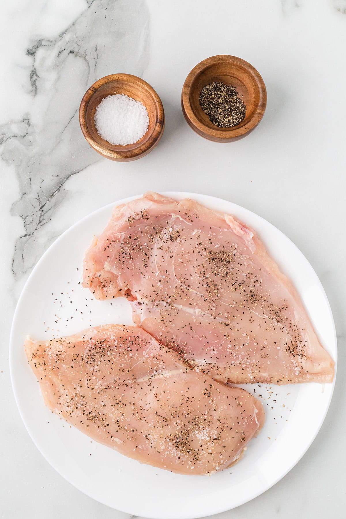 Flattened chicken breasts sprinkled with salt and pepper.