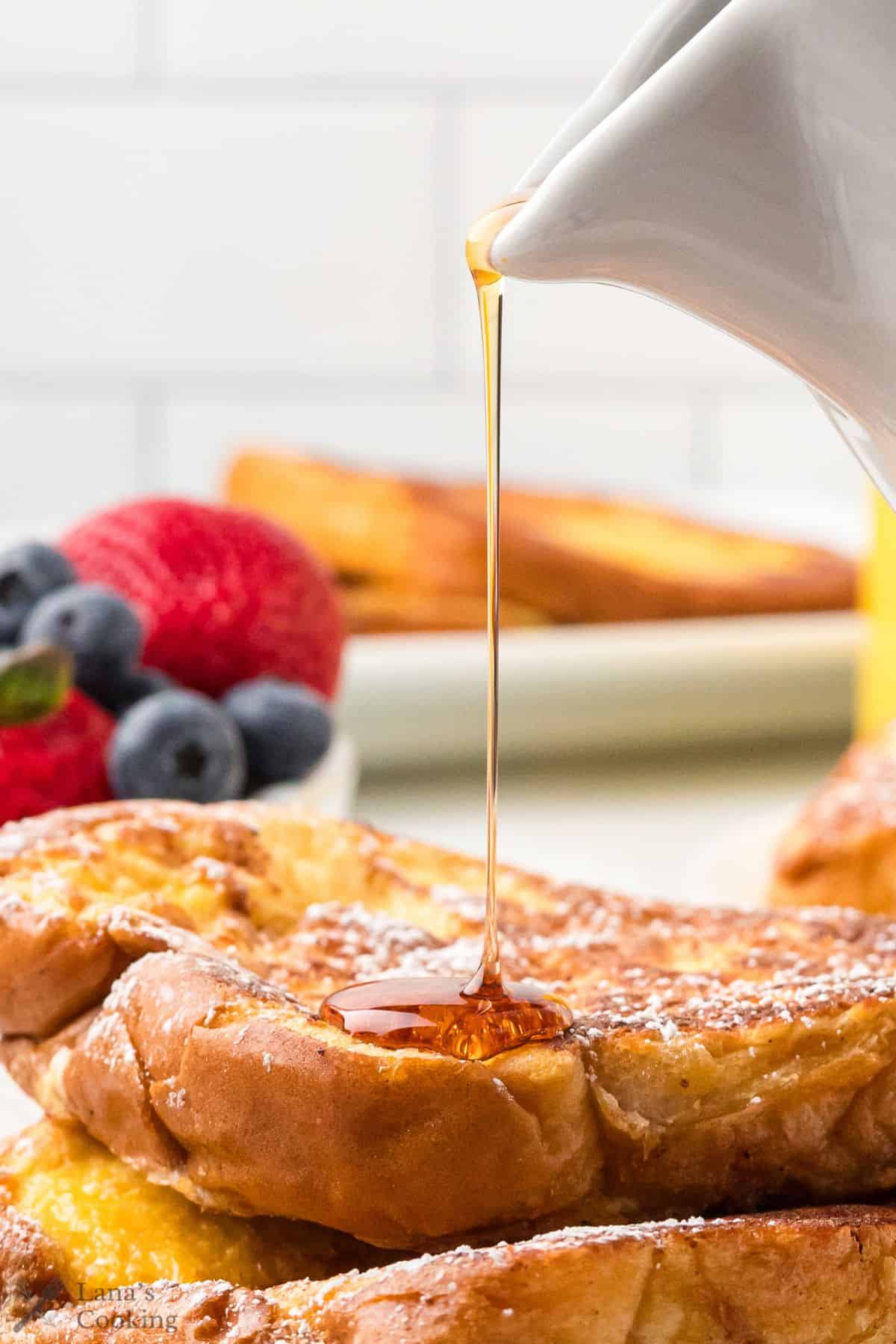 Syrup pouring from a pitcher onto slices of French toast.