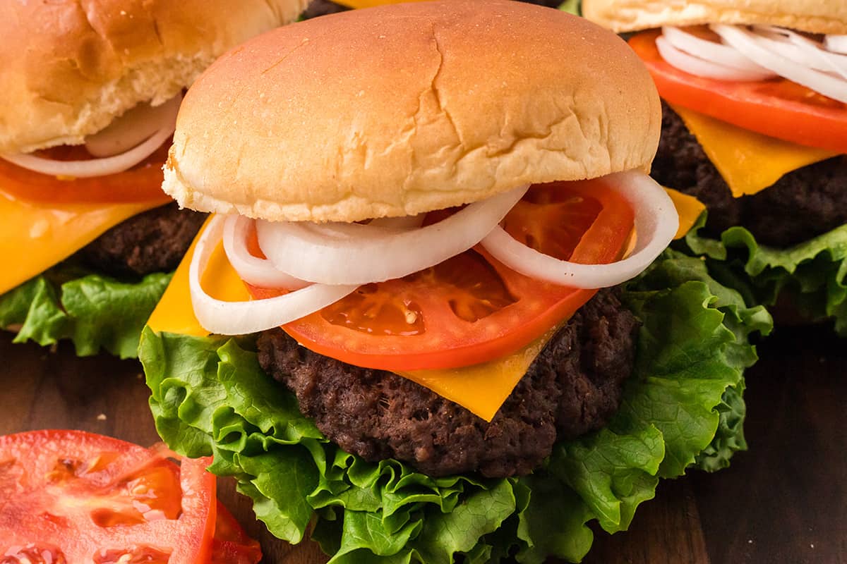 A burger on a bun with lettuce, tomato, cheese, and onions.