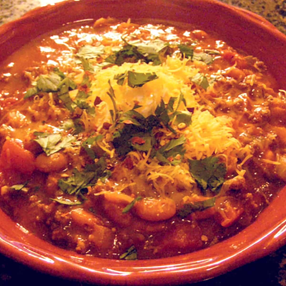 A serving of chili topped with shredded cheese in a red bowl.