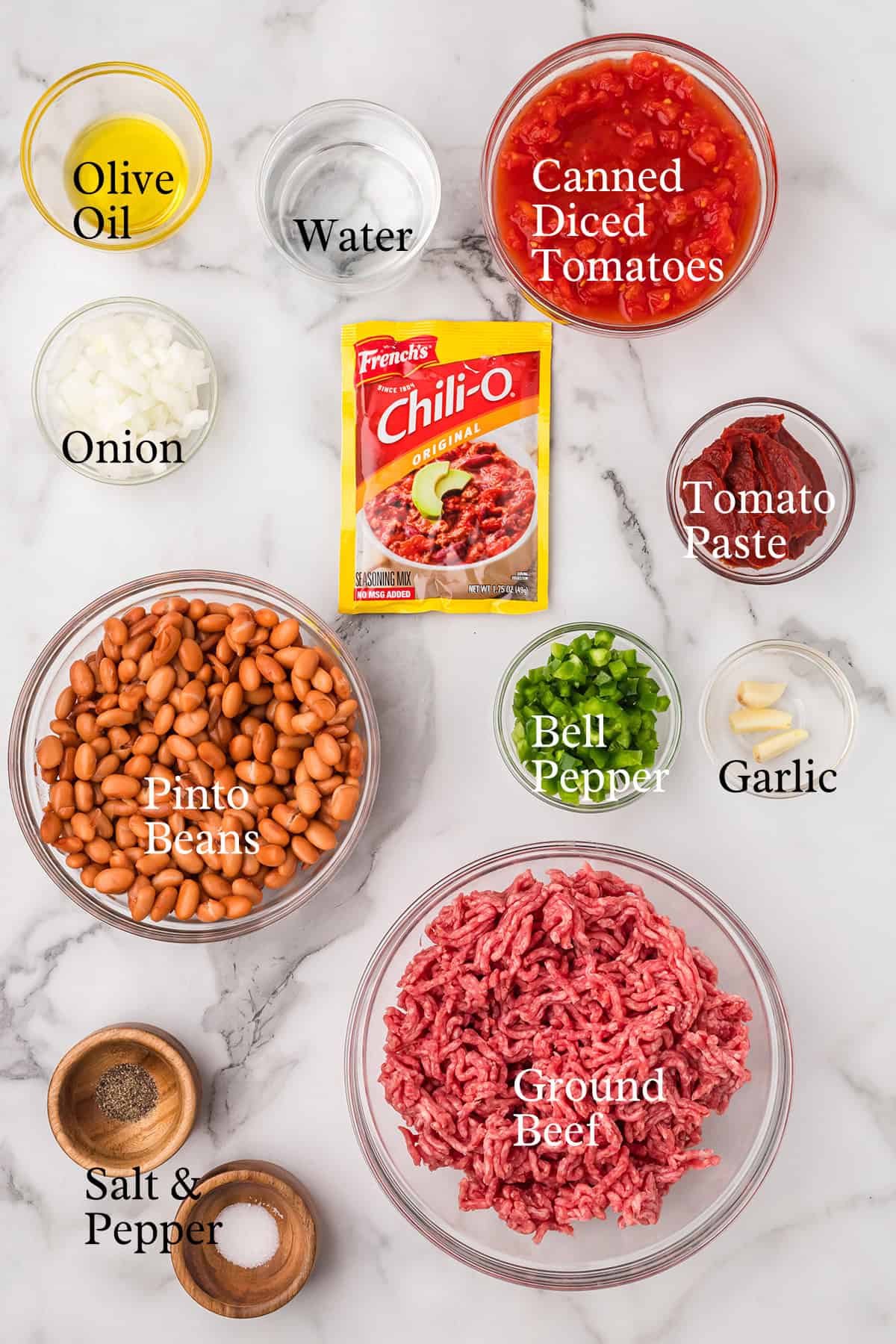 Chili ingredients in bowls on a white surface: ground beef, pinto beans, spices, canned tomatoes, and vegetables.