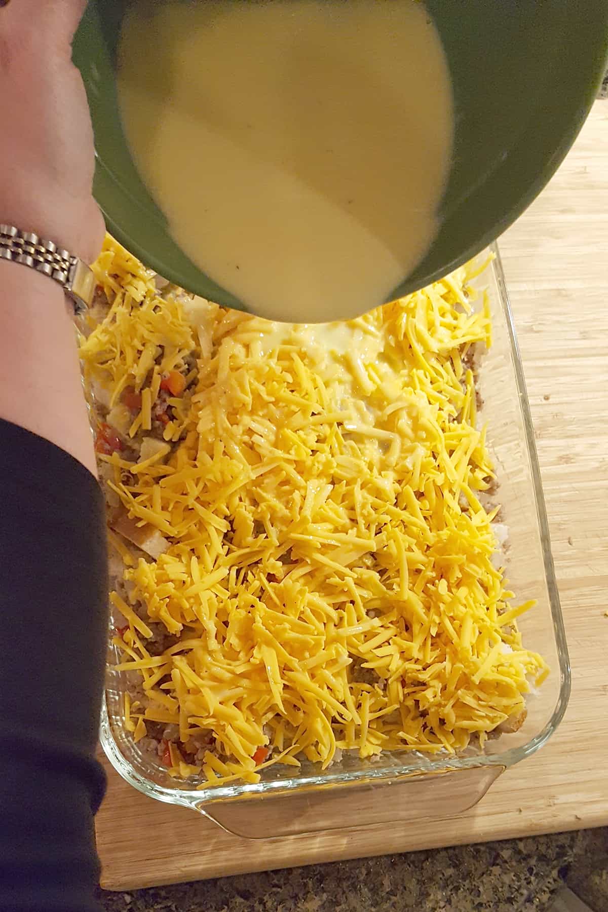 Milk and egg mixture in a mixing bowl being poured over the layered casserole.