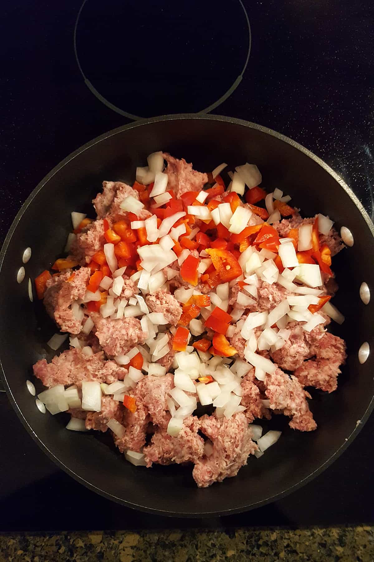 Onions, peppers, and sausage cooking in a skillet.