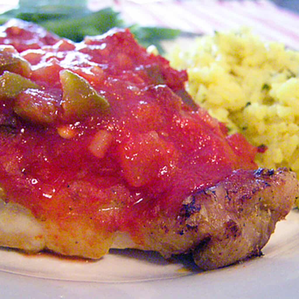 Salsa chicken with a serving of yellow rice on a white plate.
