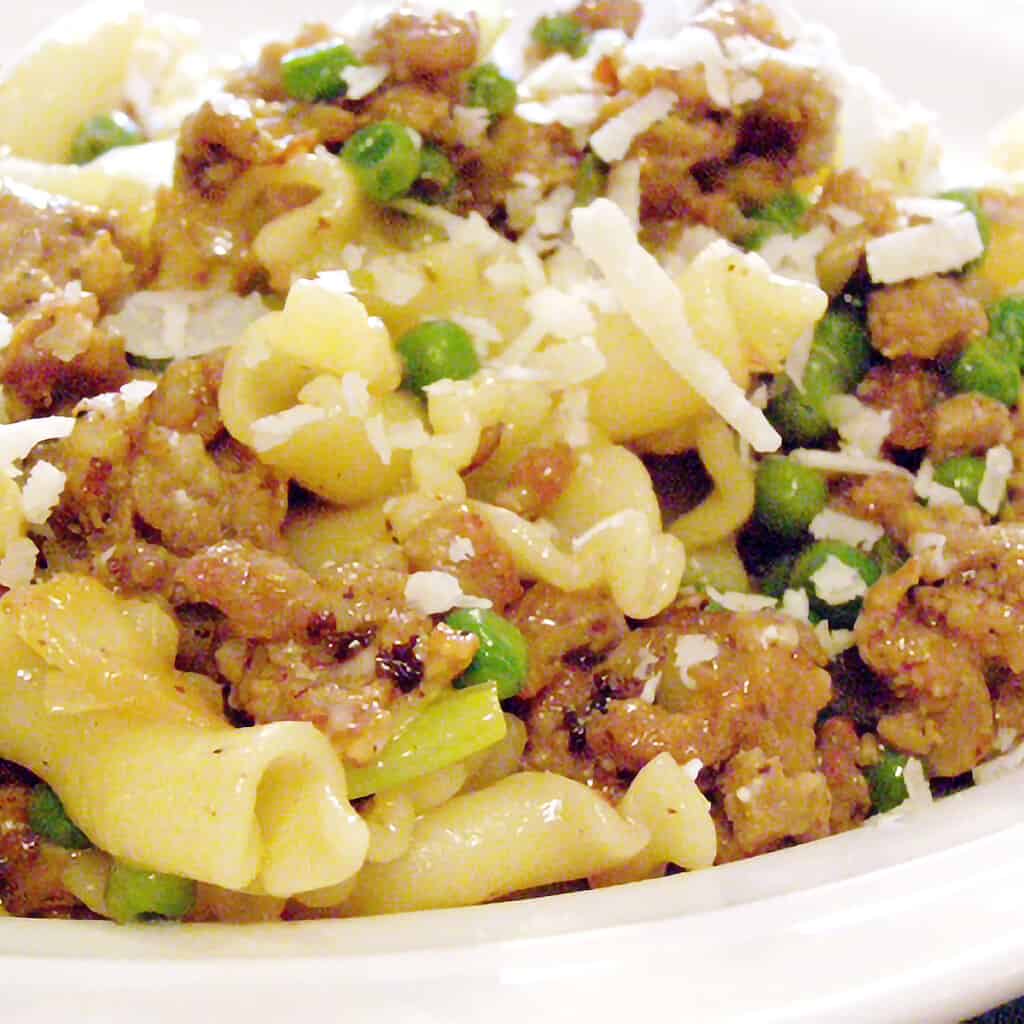 A serving of sausage and leek pasta on a white plate.