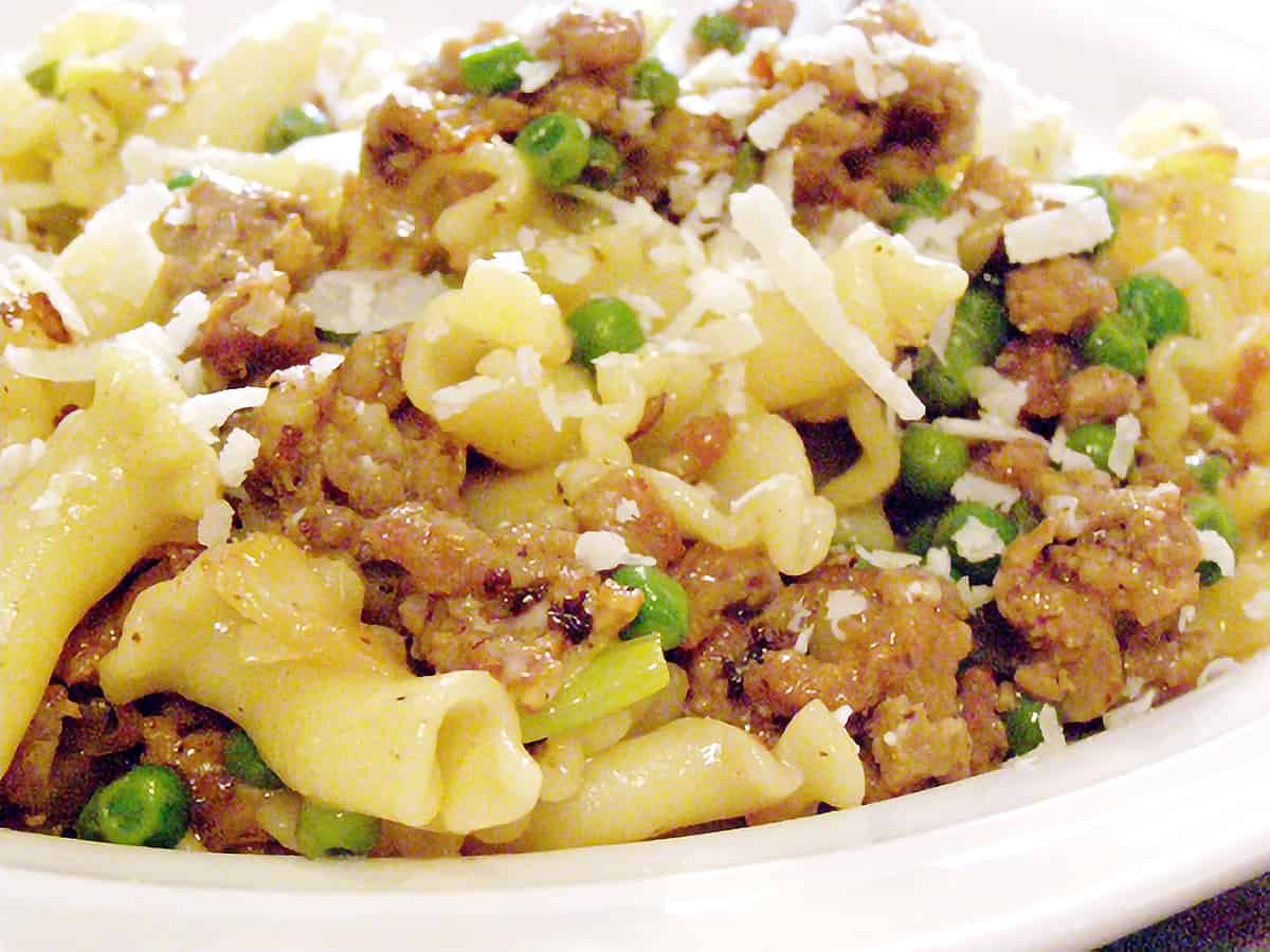 A serving of sausage and leek pasta on a white plate.
