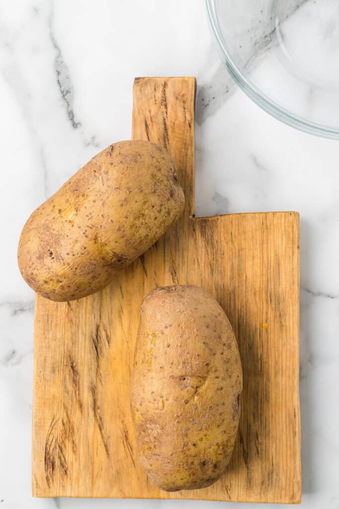 Whole baked potatoes on a board.