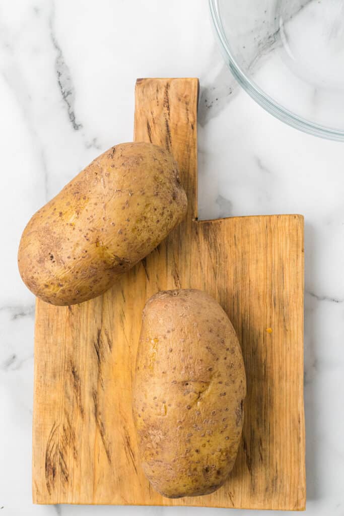 Whole baked potatoes on a board.