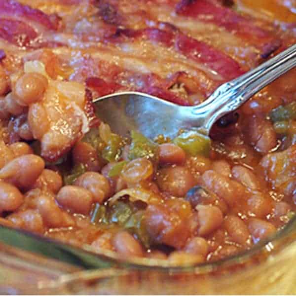 Luscious baked beans baked under a layer of bacon. Perfect side dish for barbecued spare ribs, or any summertime cookout. https://www.lanascooking.com/baked-beans/