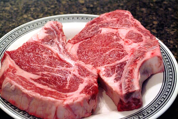 Two bone-in ribeye steaks on a plate.