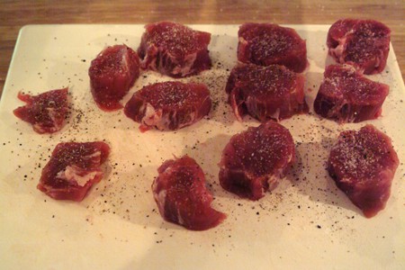 Seasoned pork tenderloin slices on a white cutting board.