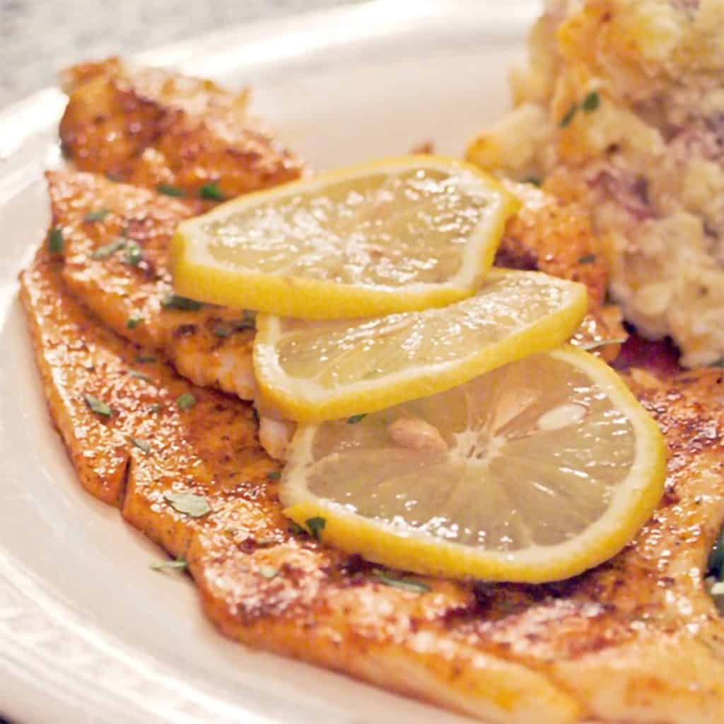 Grilled fish with lemon slices presented on a white plate.