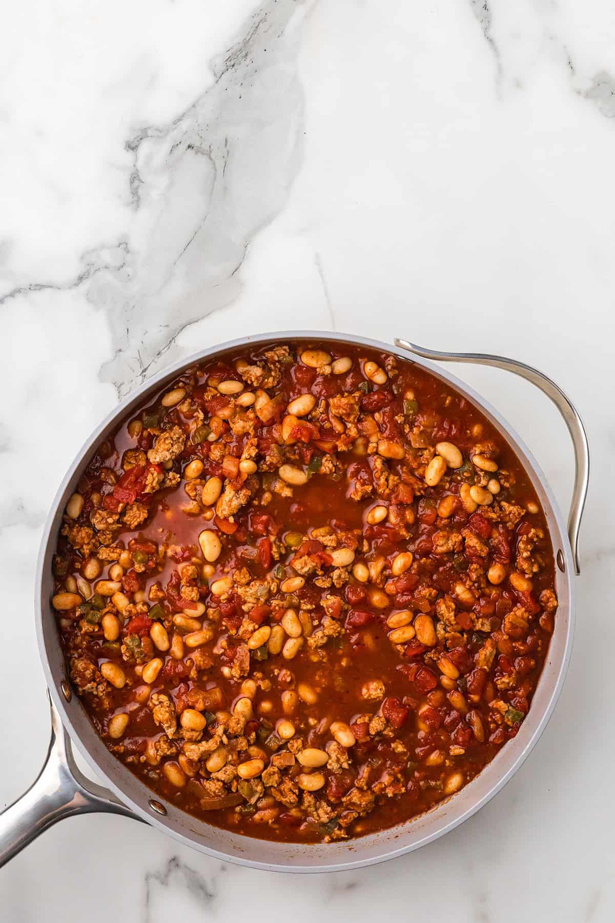 A pot of chili with beans, ground meat, and tomatoes on a marble countertop.