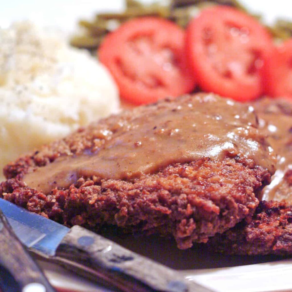 Finished country fried steak on a plate with side dishes.