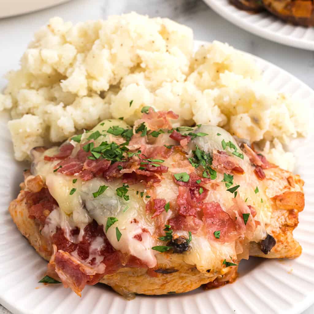 A serving of bistro chicken with mashed potatoes on a white plate.