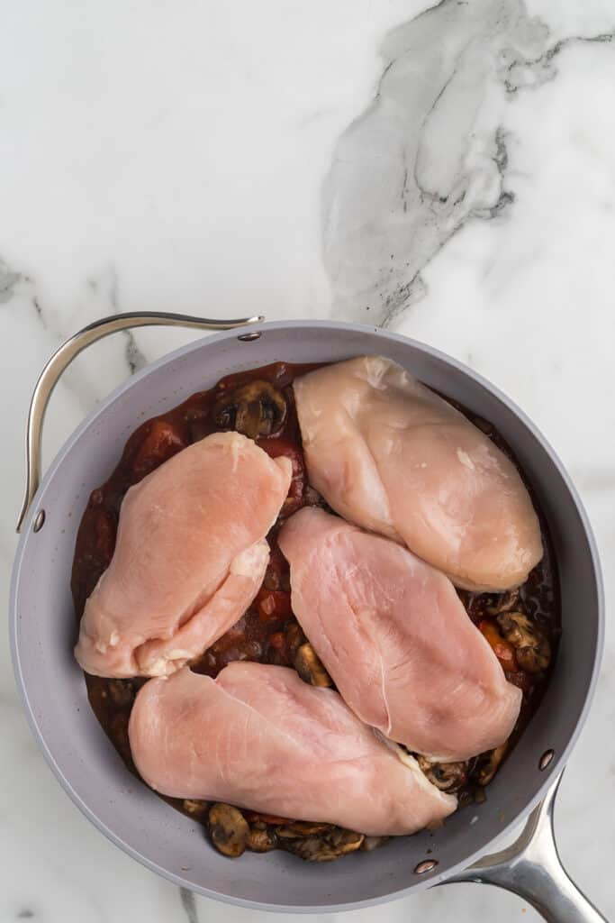 Chicken breasts added to sauce in a skillet.