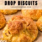 A close-up of golden-brown bacon and cheddar drop biscuits on parchment paper, with a honey dipper nearby. Text above reads, Bacon & Cheddar Drop Biscuits and lanascooking.com.
