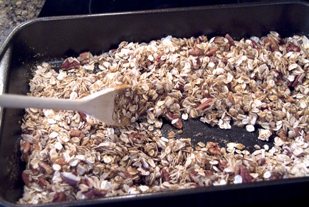 Stirring the wet ingredients into the oats and nuts in a baking pan.