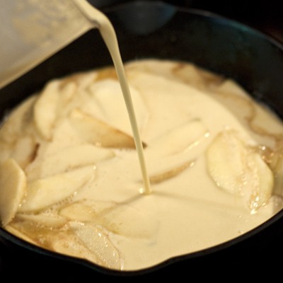 Pouring the batter over the apples in the skillet.