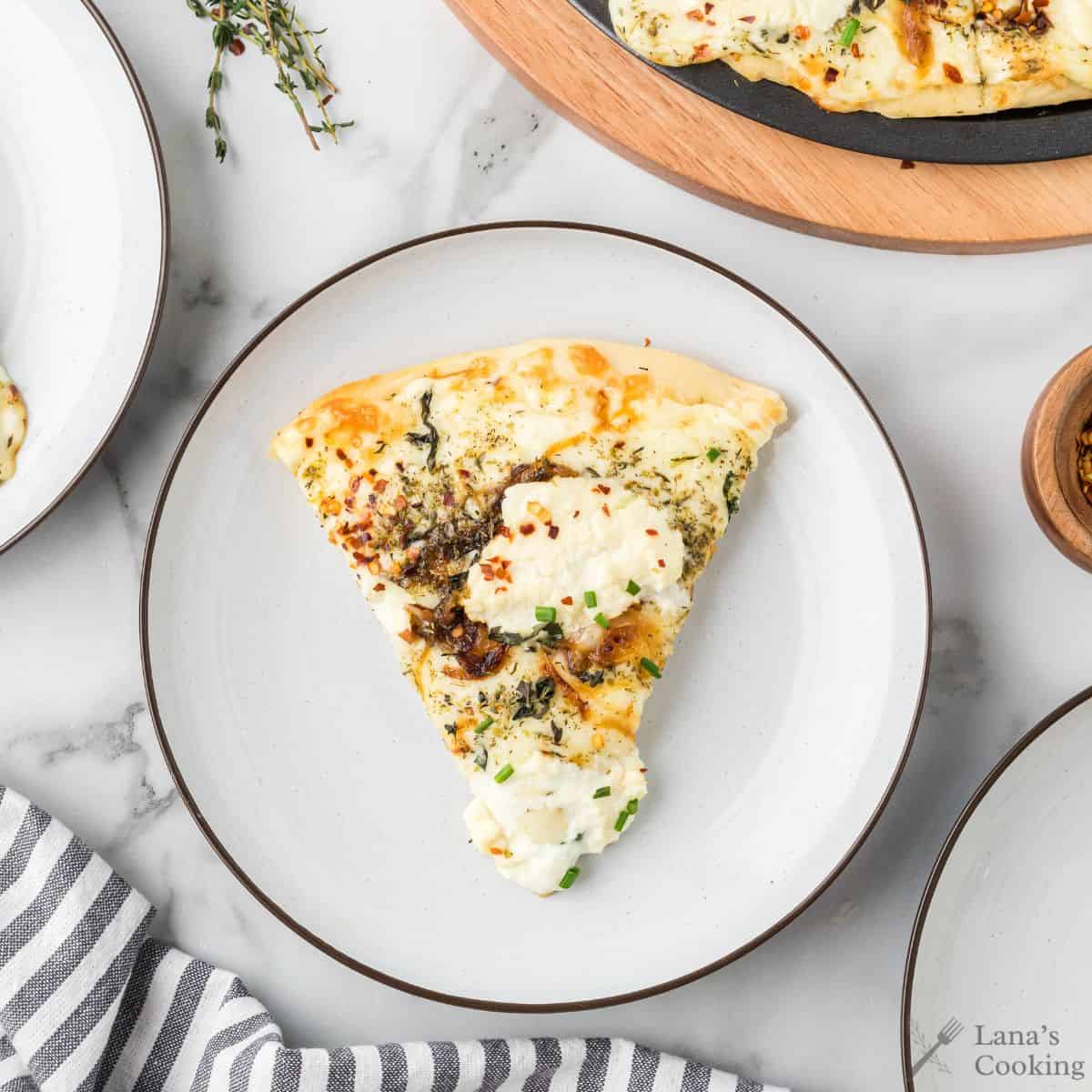 A slice of white pizza with ricotta cheese, herbs, and caramelized onions on a white plate, viewed from above.