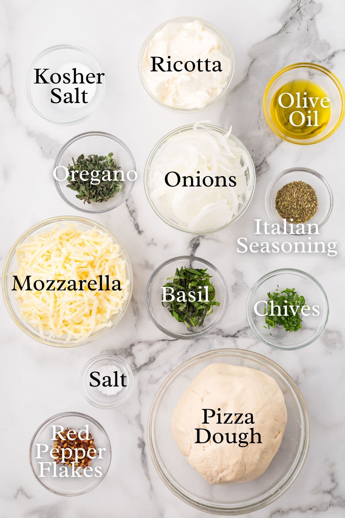 Top-down view of ingredients for pizza dough and toppings: ricotta, olive oil, mozzarella, salt, herbs (oregano, basil, chives), onions, Italian seasoning, red pepper flakes, and kosher salt.