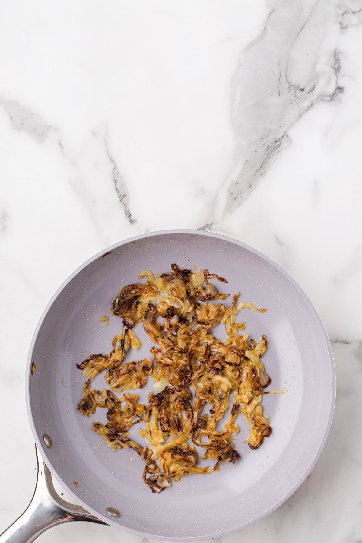 A frying pan with caramelized onions on a white marble countertop.