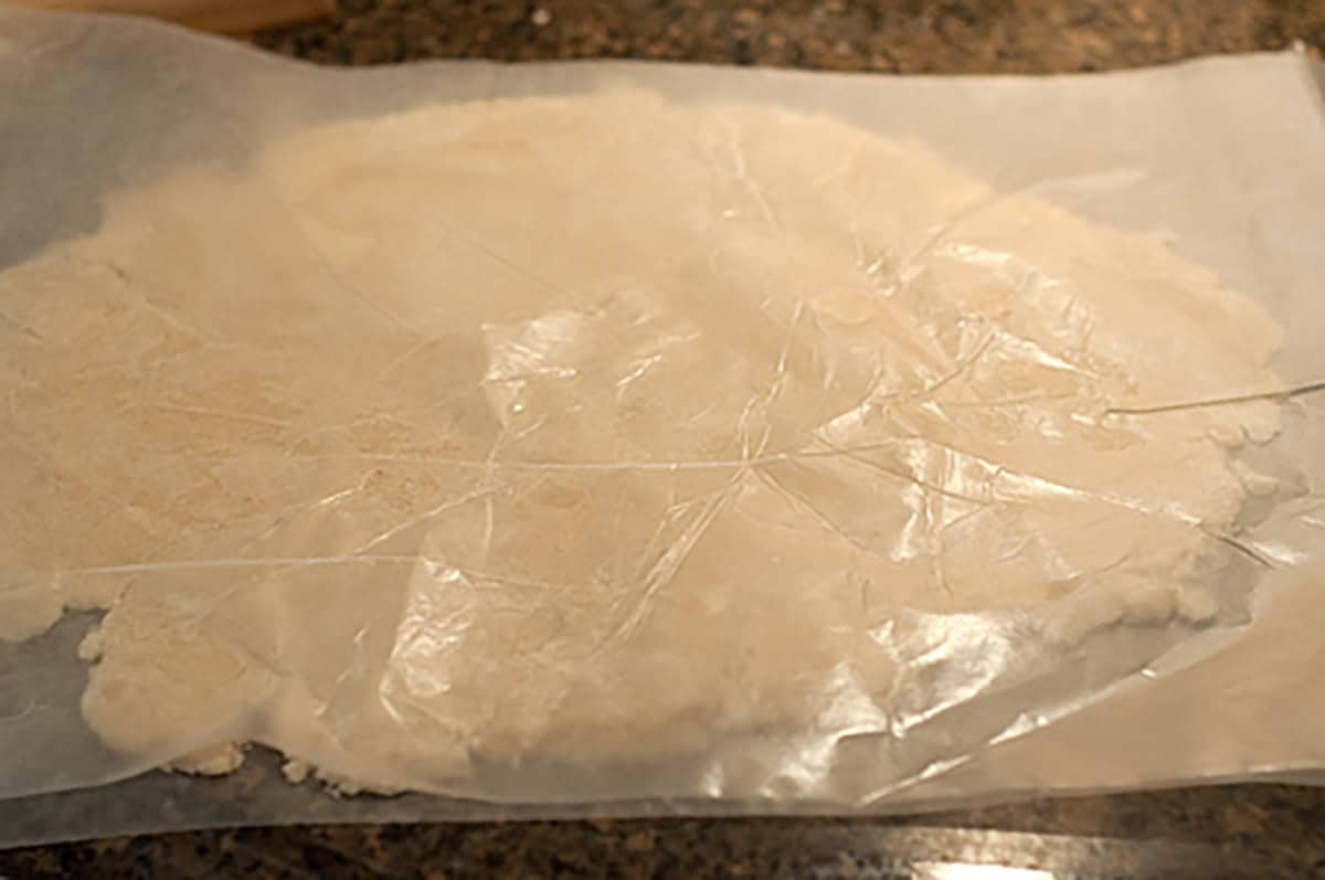 Rolled-out dough for an apricot thyme galette rests between two sheets of wax paper on a kitchen countertop.