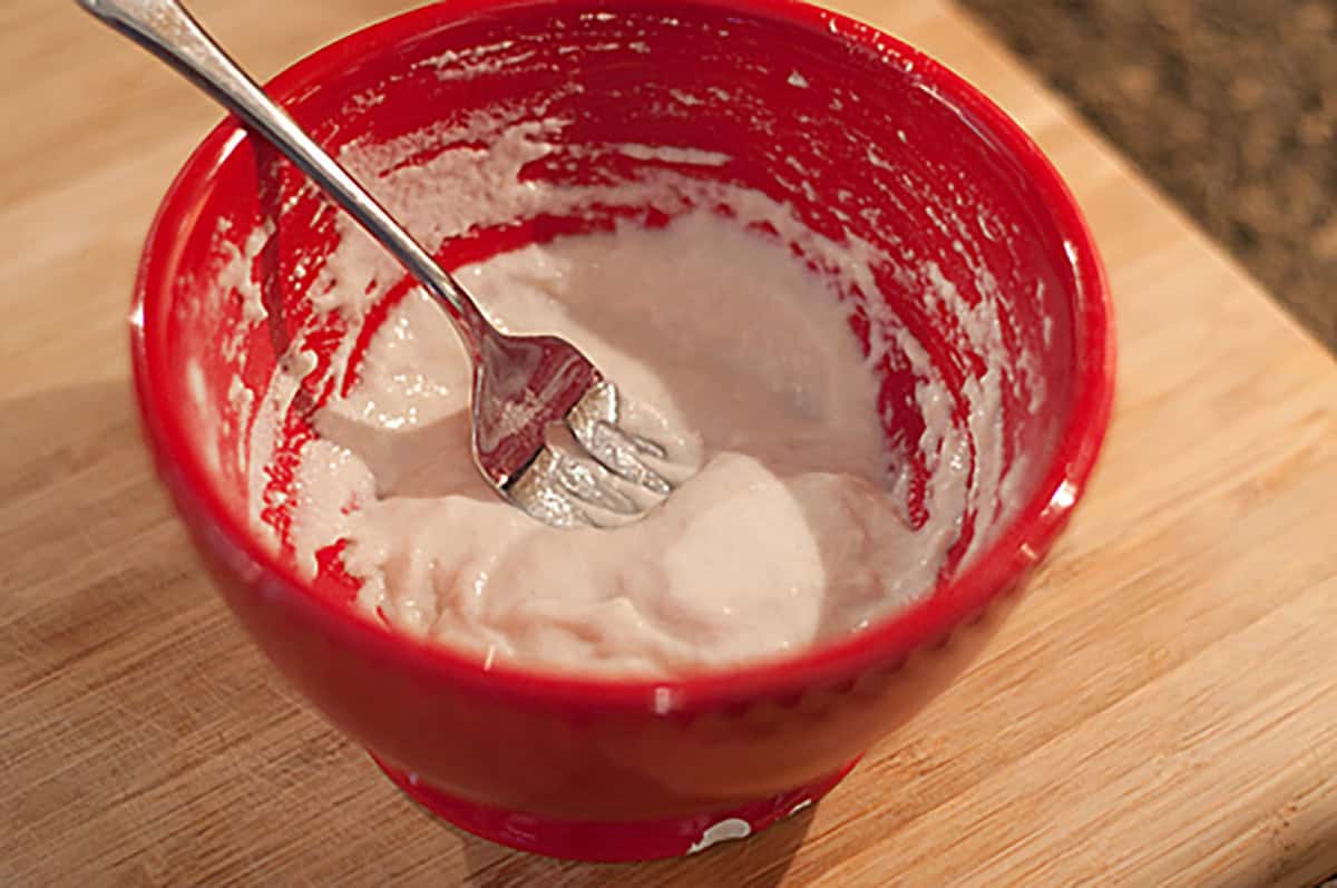 A red bowl with the slurry mixture and a fork inside, sitting on a wooden surface.