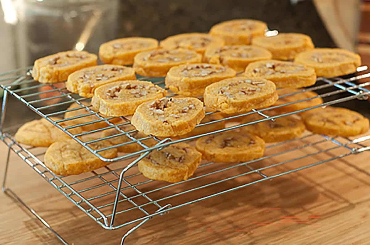 Two wire cooling racks stacked with freshly baked pinwheels topped with chopped nuts on a wooden surface.