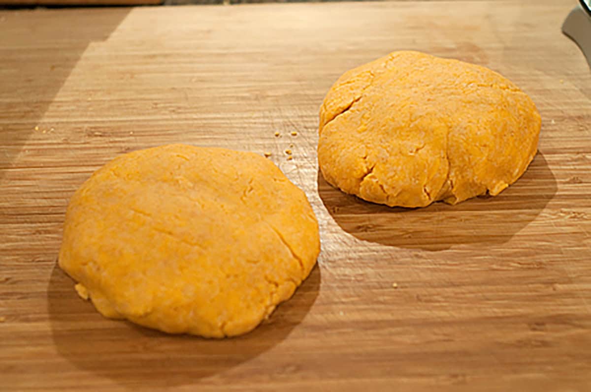 Two round discs of orange dough rest on a wooden surface.