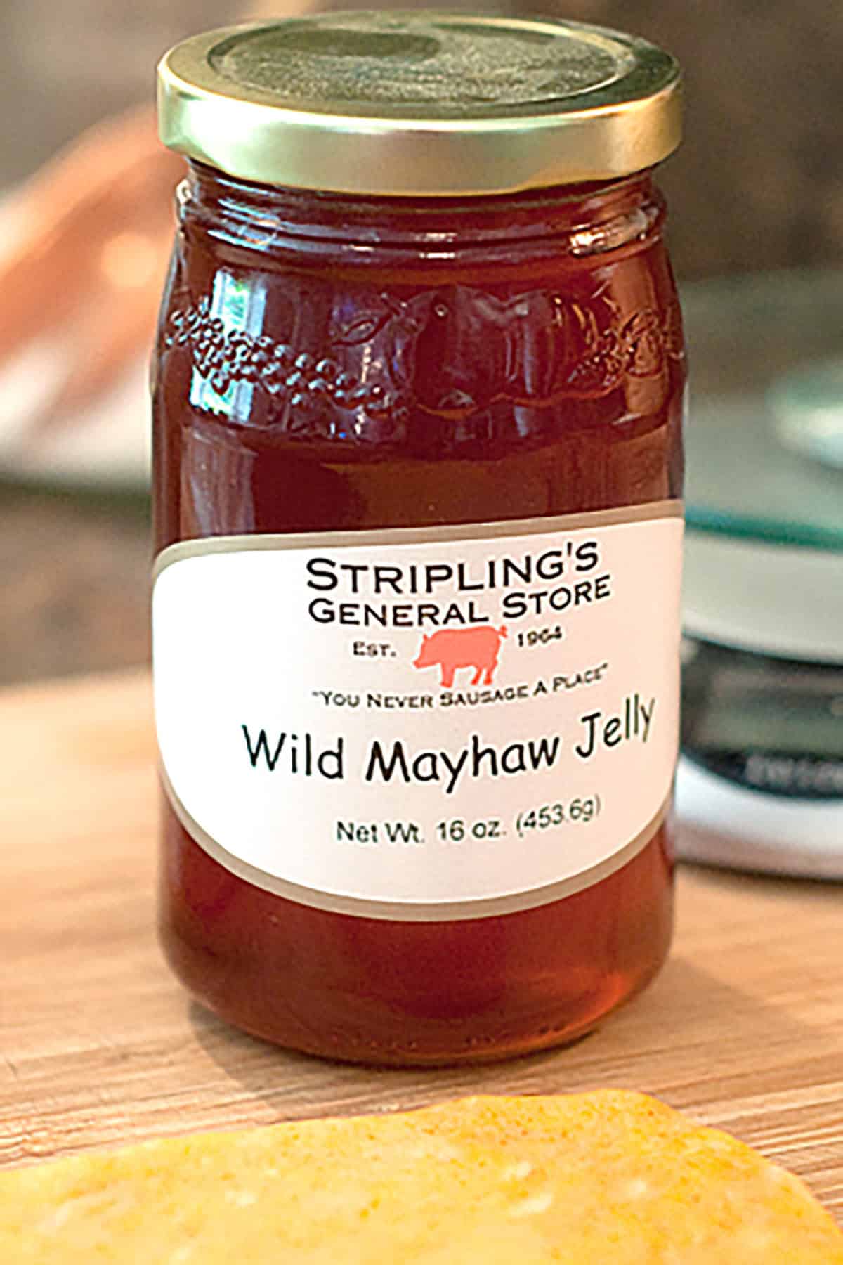 A 16-ounce jar of Stripling&rsquo;s General Store Wild Mayhaw Jelly with a gold lid sits on a wooden surface.