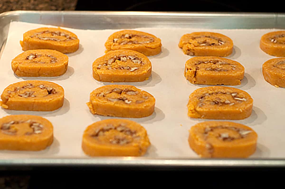 Slices of unbaked pinwheel dough with nuts are arranged on a parchment-lined baking sheet, ready to be baked.