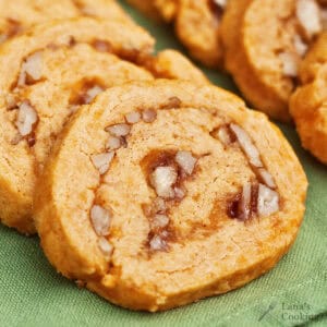 Close-up of sliced pinwheel cookies with visible chopped pecans and a swirl of filling, arranged on a green surface.