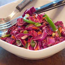 A serving of slaw in a white bowl with a fork.