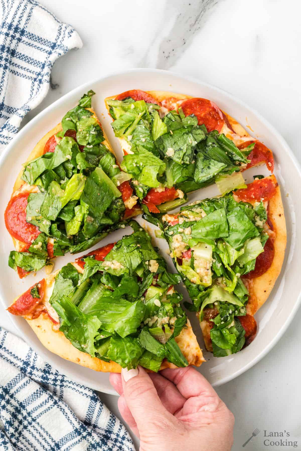 Caesar salad pizza on a white plate after being sliced into four pieces.