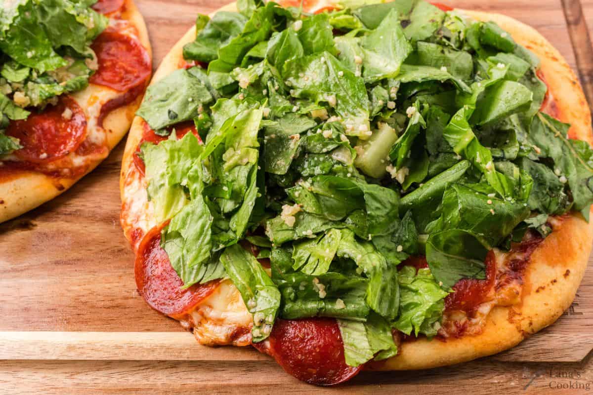 Finished Caesar Salad Pizzas with pepperoni on a wooden cutting board before being sliced.