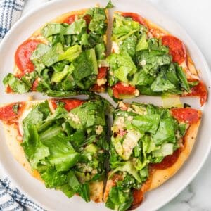 Close-up photo of pepperoni pizza with caesar salad on top.