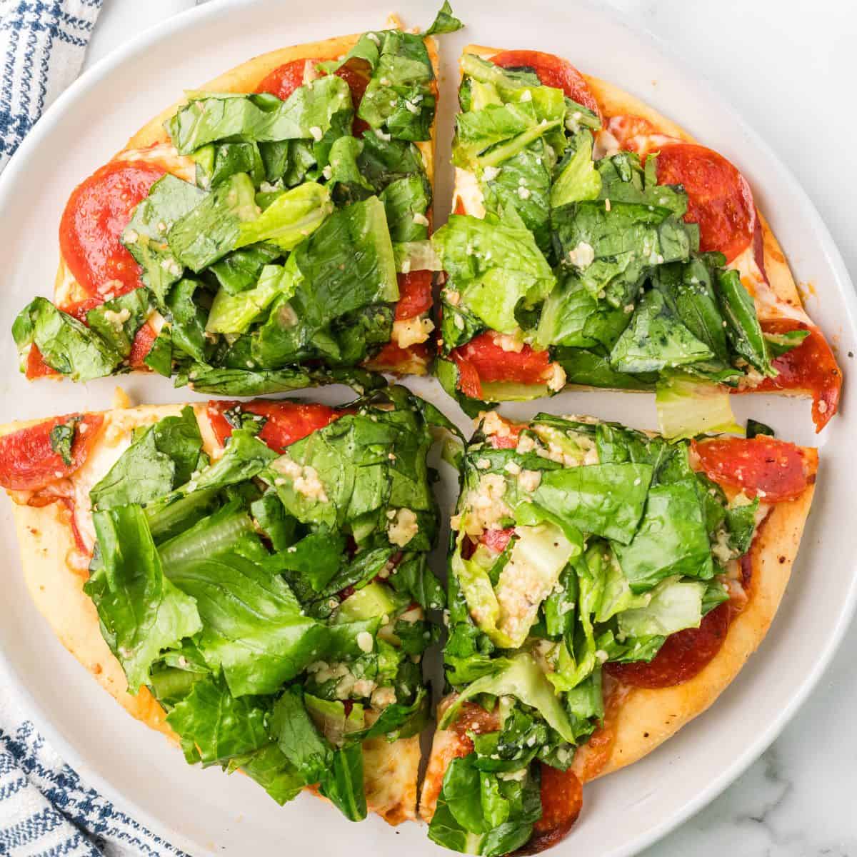 Close-up photo of pepperoni pizza with caesar salad on top.