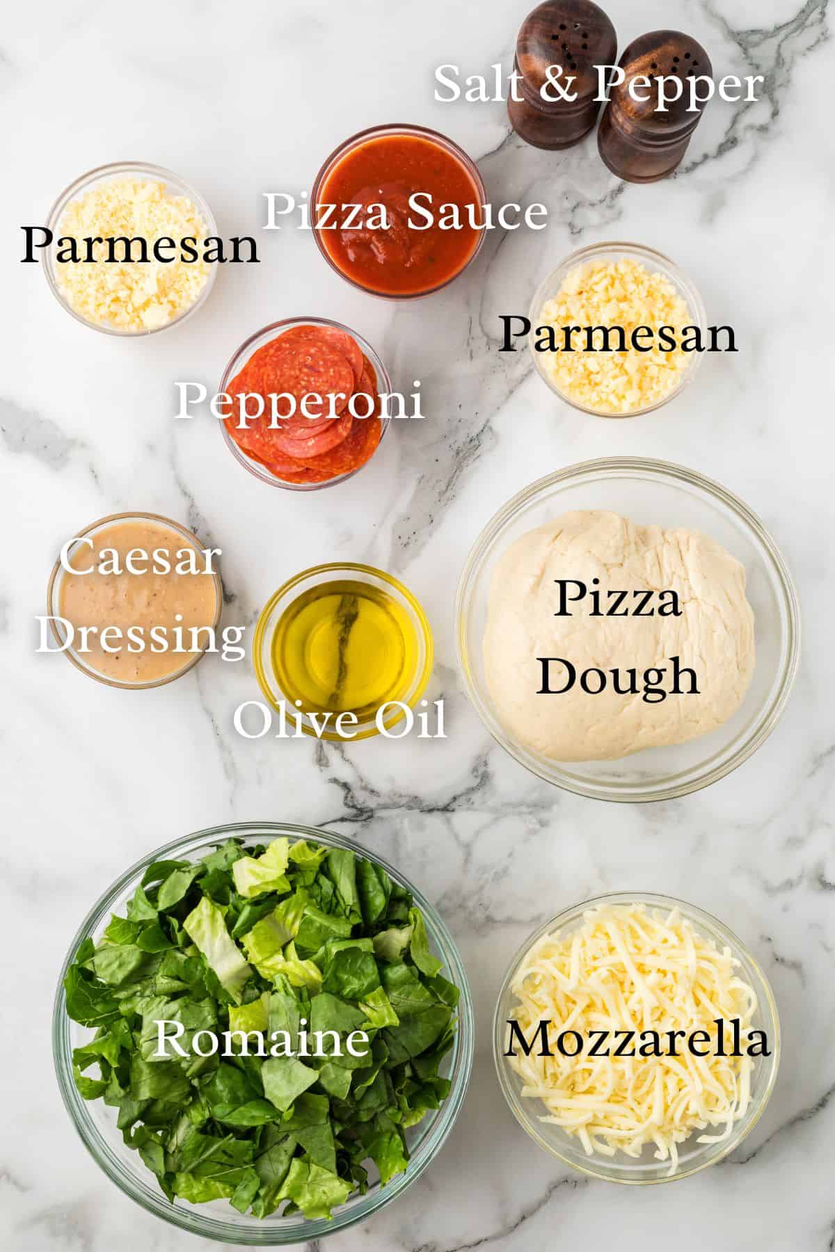Ingredients for Caesar Salad Pizza on a white marble background in individual containers.