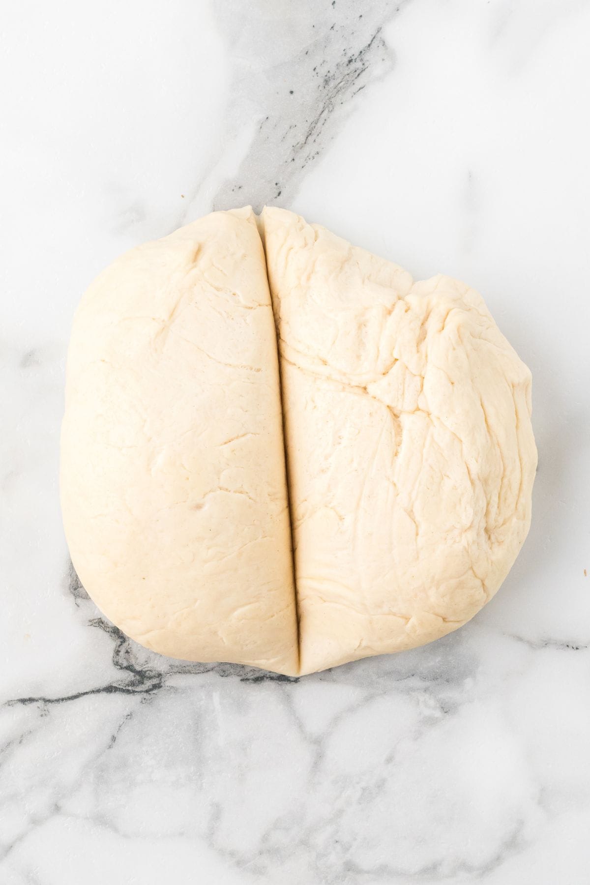 A ball of dough split in half sits on a white marble surface.