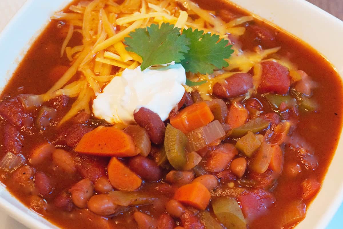 Bowl of chili topped with shredded cheese, sour cream, and cilantro.