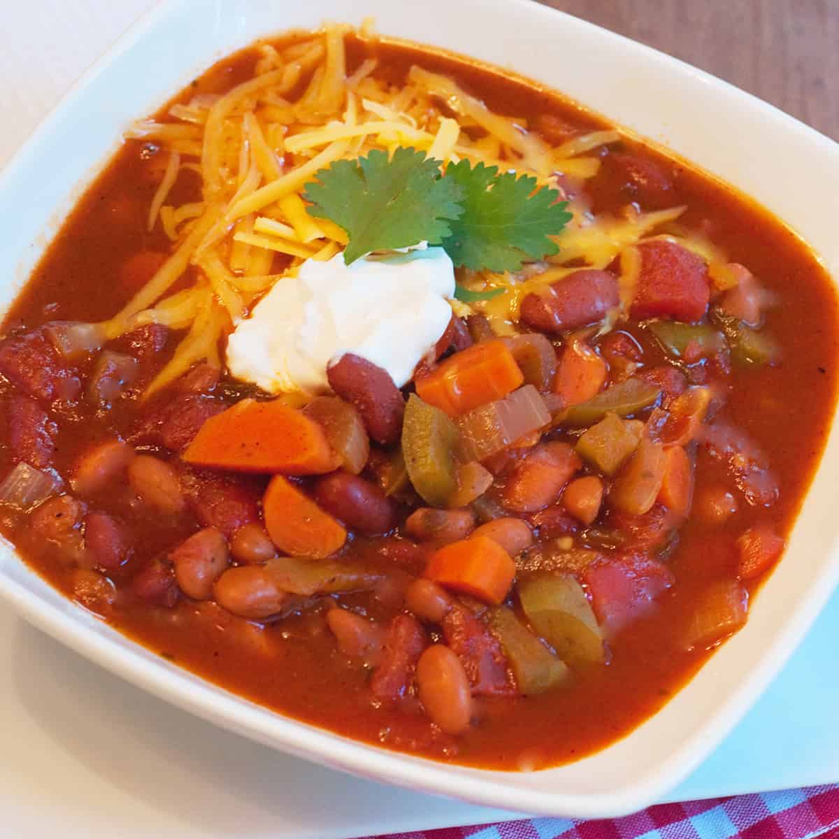A bowl of chili topped with shredded cheese, sour cream, and cilantro, with beans and vegetables visible.