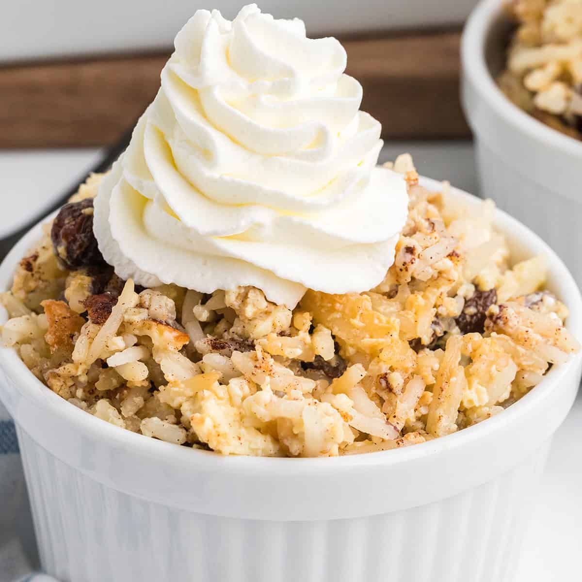 Baked rice pudding in a small ramekin with a swirl of whipped cream on top.