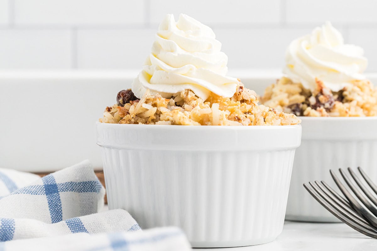 Baked rice pudding in a small ramekin with a swirl of whipped cream on top.