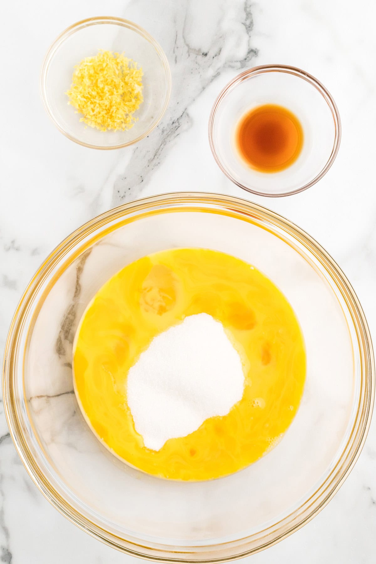 A mixing bowl holding eggs, salt, sugar, vanilla, and lemon rind.