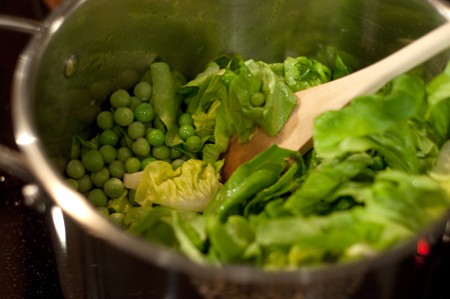 Combining peas and lettuce in a saucepan.