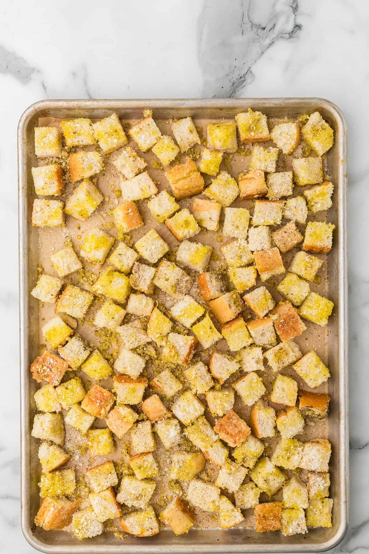Cubed bread tossed with oil and seasoning on a baking sheet, ready to be baked into croutons.