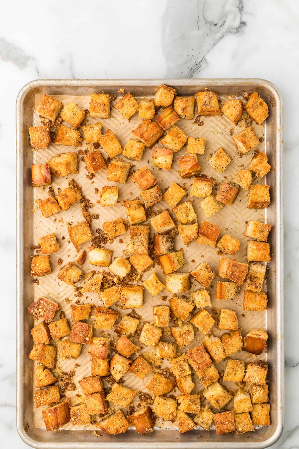 A baking sheet with golden-brown homemade croutons spread out on parchment paper.