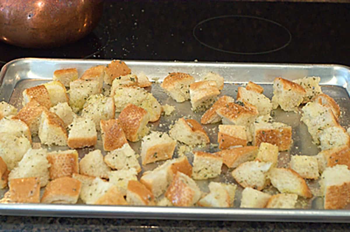 Cubed pieces of bread seasoned and spread on a baking sheet, ready to be toasted for croutons.